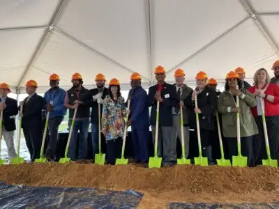 A line of people wearing orange Roseburg hardhats pose with shovels and a pile of dirt.