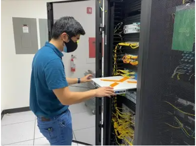 A male inserts a piece of equipment into a server rack